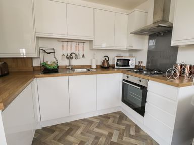 A kitchen with white cabinets wooden countertops a sink a microwave a kettle an oven and a stove at Manor Heath Apartment 1 in Scarborough