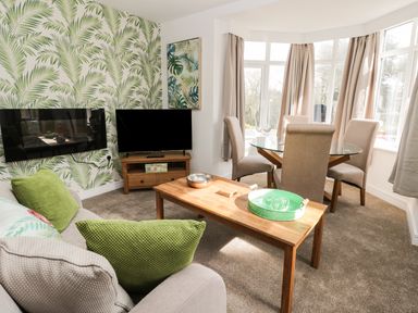 A living room with a sofa green cushions wooden coffee table wall mounted tv and dining table with chairs at Manor Heath Apartment 1 Scarborough