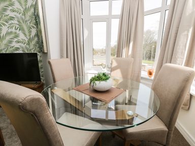 A dining area with a glass round table four beige chairs and a plant on the table by a bay window at Manor Heath Apartment 1 in Scarborough