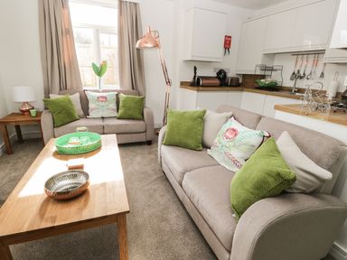 A living room with beige sofas and green cushions next to a kitchen area at Manor Heath Apartment 1 in Scarborough