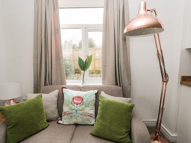 A beige sofa with green and floral cushions under a window with beige curtains beside a copper floor lamp at Manor Heath Apartment 1 in Scarborough