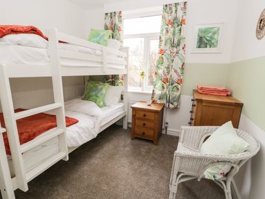 A bedroom with white bunk beds a wooden nightstand wooden dresser and a white wicker chair at Manor Heath Apartment 1 in Scarborough