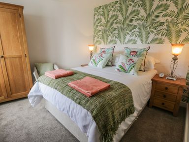 A bedroom with a double bed cushions and towels bedside tables lamps a wardrobe and a chair at Manor Heath Apartment 1 in Scarborough
