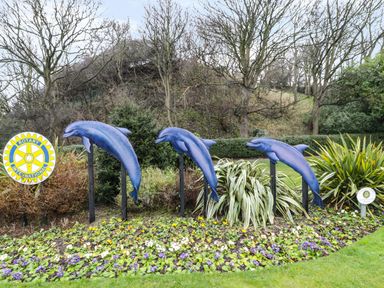 A garden with blue dolphin sculptures and flowers with trees and shrubs at Manor Heath Apartment 1 in Scarborough