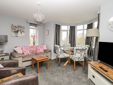 A living room with a sofa, armchairs, a dining table with chairs, windows with curtains, and a television at Manor Heath Apartment 4 in Scarborough