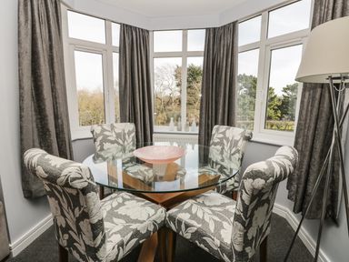 A dining area with a round glass table and four patterned chairs next to windows with dark curtains at Manor Heath Apartment 4 in Scarborough