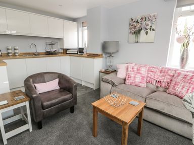 A living room and kitchen area with grey armchair and sofa with pink cushions at Manor Heath Apartment 4 in Scarborough