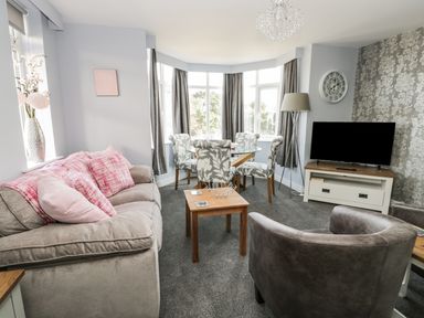 A living room with a sofa and armchair a dining table with chairs a TV and a floor lamp at Manor Heath Apartment 4 in Scarborough