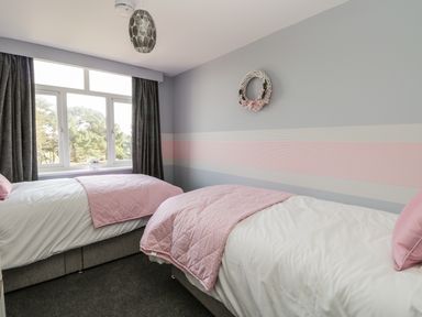 A bedroom with two single beds covered with pink blankets and white sheets and a window with dark curtains at Manor Heath Apartment 4 in Scarborough