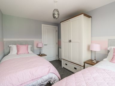 A bedroom with two single beds pink bedding and pillows a white wardrobe and bedside tables with lamps at Manor Heath Apartment 4 Scarborough