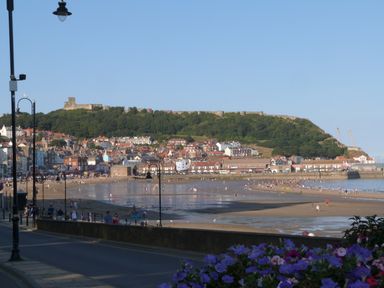 A beach with people walking near a town and a hill with a castle in the background at Manor Heath Apartment 4 in Scarborough