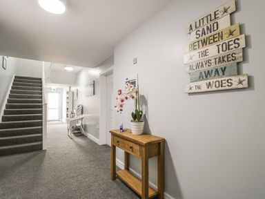 A hallway with carpeted stairs a wooden table with a plant and a wall sign at Manor Heath Apartment 4 in Scarborough