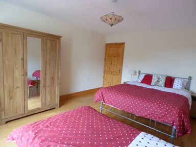 A bedroom with two beds with red polka dot bedding a wooden wardrobe with a mirror and a wooden door at The Slate House in Cahersiveen County Kerry