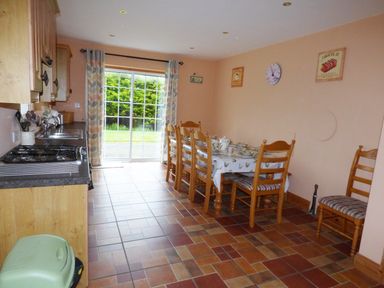 A kitchen dining area with wooden cabinets a long dining table with chairs and a sliding glass door at The Slate House in Cahersiveen County Kerry