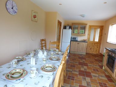 A kitchen with a dining table set with dishes and cups wooden chairs tiled floor and wooden cabinets at The Slate House in Cahersiveen County Kerry
