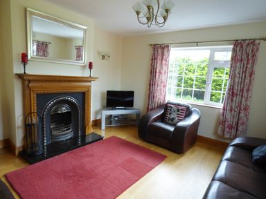 A living room with a fireplace a red rug a brown armchair a sofa a TV and floral curtains at The Slate House in Cahersiveen County Kerry