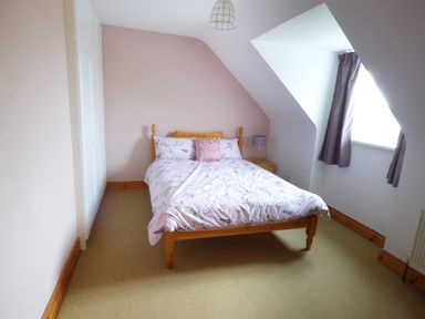 A bedroom with a wooden bed with floral bedding a bedside table with a lamp window with curtains and built in white wardrobes at The Slate House in Cahersiveen County Kerry