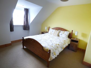 A bedroom with a wooden double bed floral bedding two bedside tables with lamps and a window with curtains at The Slate House in Cahersiveen County Kerry