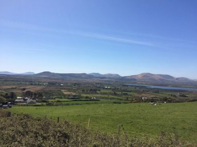 A rural landscape with green fields, scattered houses, grazing sheep, and mountains in the background at The Slate House in Cahersiveen County Kerry