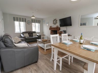 A living room with gray sofas a wooden coffee table a fireplace wall-mounted TV and a dining table with chairs at Flip Flops The Bay near Filey