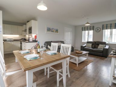 An open plan kitchen and living area with a wooden dining table set with plates and wine glasses two grey sofas and a coffee table at Flip Flops The Bay near Filey