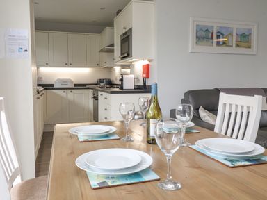 A kitchen with white cabinets and a dining table set with plates wine glasses and a bottle at Flip Flops in The Bay near Filey