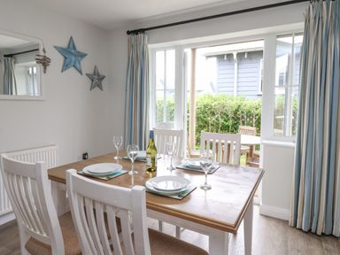 A dining table set for four with plates and wine glasses near glass doors with striped curtains at Flip Flops in The Bay near Filey