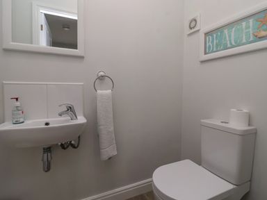 A small bathroom with a wall-mounted sink a towel ring with a towel a toilet with a roll of toilet paper and a framed beach sign on the wall at Flip Flops The Bay near Filey