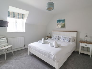 A bedroom with a double bed, two bedside tables, a wall-mounted television, and a window with striped blinds at Flip Flops The Bay near Filey