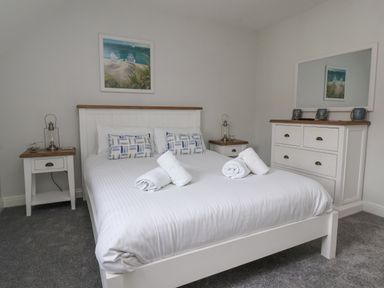 A bedroom with a white bed and rolled towels two bedside tables and a dresser with a mirror at Flip Flops in The Bay near Filey