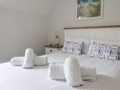 A bedroom with a bed made with white linens and rolled white towels on the bed a nightstand with a lantern and a painting above the bed at Flip Flops The Bay near Filey