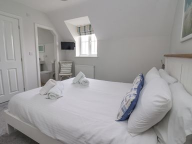 A bedroom with a double bed white bedding rolled towels and pillows a window chair and ensuite bathroom at Flip Flops The Bay near Filey
