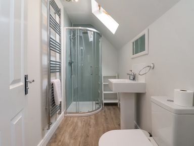 A bathroom with a corner shower, white sink, toilet, towel radiator, and skylight at Flip Flops in The Bay near Filey
