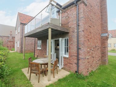A brick house with a patio table and four wooden chairs under a balcony with glass railing at Flip Flops The Bay near Filey