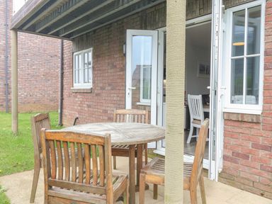 A wooden table with four wooden chairs on a patio outside a brick house with white doors and windows at Flip Flops in The Bay near Filey
