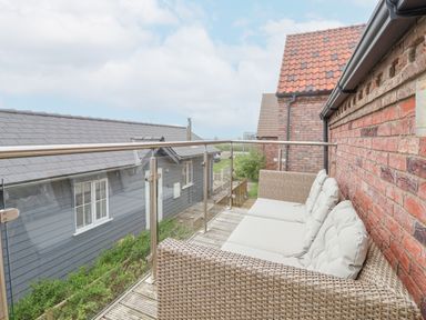 A balcony with a wicker sofa with cushions and glass railing overlooking neighboring houses at Flip Flops in The Bay near Filey