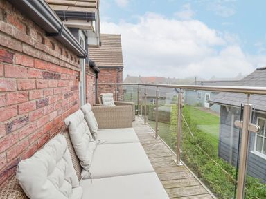 A balcony with cushioned wicker seating and glass railing overlooking neighboring houses at Flip Flops in The Bay near Filey