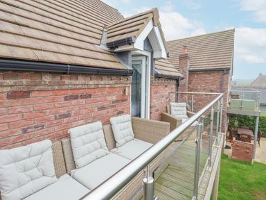 A balcony with cushioned wicker seating and glass railing attached to a brick house at Flip Flops The Bay near Filey