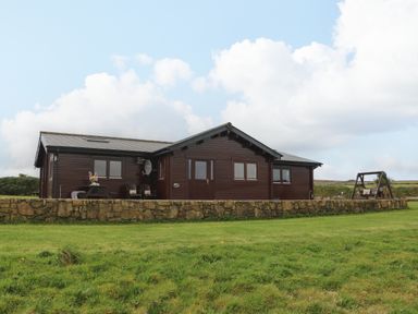 A single story wooden house with a stone wall in front and a swing on the right at Chywolow Lodge in Penzance