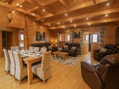 A wooden lodge living room with a dining table set with plates and glasses and leather sofas and armchairs at Chywolow Lodge in Penzance