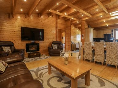 A living room with brown leather sofas a wooden coffee table and a dining table with chairs in a wooden cabin at Chywolow Lodge in Penzance