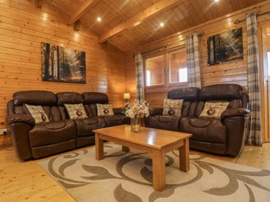 A living room with two brown leather sofas a wooden coffee table with flowers and a patterned rug at Chywolow Lodge in Penzance