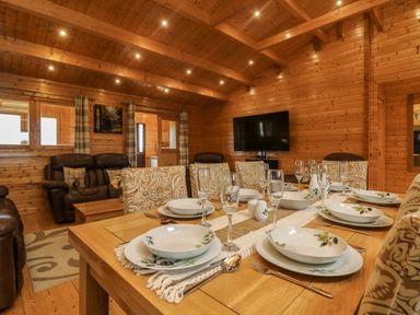 A dining table set with plates glasses and cutlery in a wooden lodge living area at Chywolow Lodge in Penzance