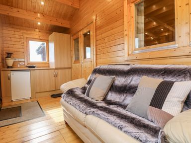 A wooden cabin interior with a cream sofa covered with a blanket and two pillows at Chywolow Lodge in Penzance