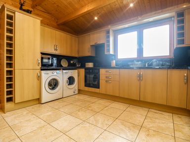 A kitchen with wooden cabinets two washing machines a microwave an oven and a window at Chywolow Lodge in Penzance