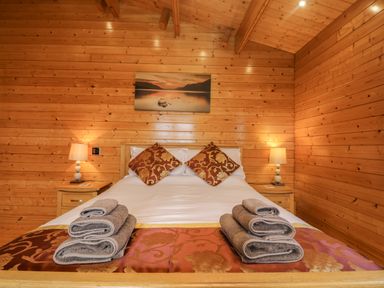 A wooden bedroom with a double bed two pillows two stacks of towels two bedside tables and lamps at Chywolow Lodge in Penzance