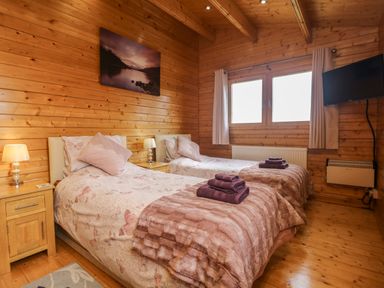 A bedroom with two single beds with bedside tables lamps and a wall-mounted television at Chywolow Lodge in Penzance