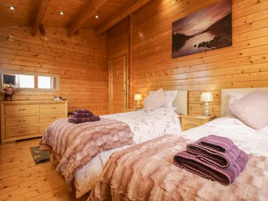 A bedroom with two single beds with folded towels on them wooden walls and ceiling a wooden dresser with a mirror and a door on the wall at Chywolow Lodge in Penzance