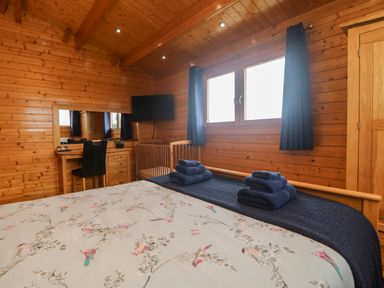 A bedroom with a bed folded towels a wooden wardrobe a crib a desk with a chair and a wall-mounted TV at Chywolow Lodge in Penzance