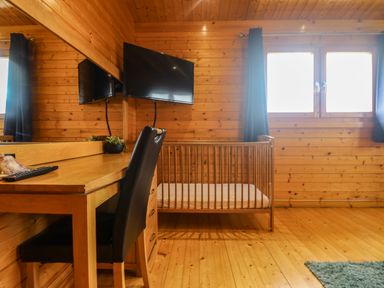 A wooden room with a crib desk chair wall mounted TV and windows at Chywolow Lodge in Penzance